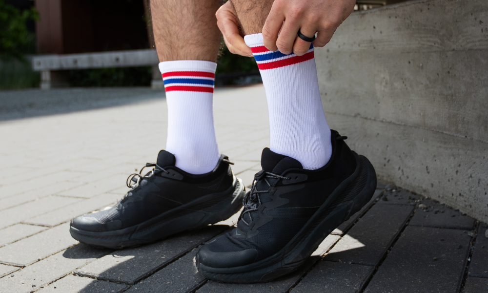 Person pulling on white athletic crew socks with red and blue stripes before a run