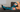 Person resting on a couch wearing OUTWAY teal knee-high compression socks with tree and sunset pattern