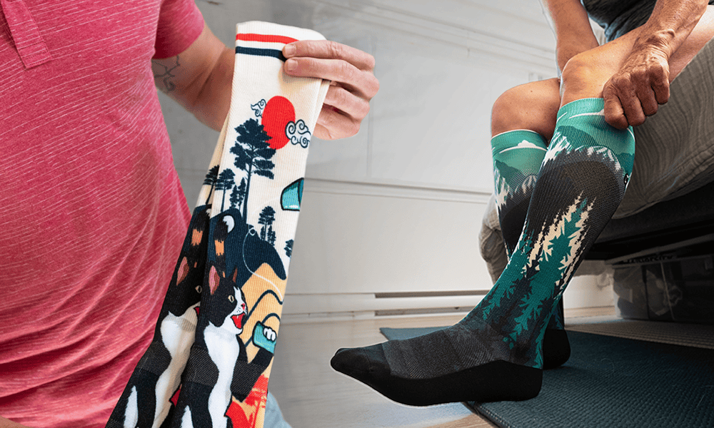 Two pairs of colorful knee-high socks. On the left, a cream sock featuring a Japanese-inspired design with cats, trees, and a red sun. On the right, a person wearing teal and grey socks with a mountain and forest landscape design.