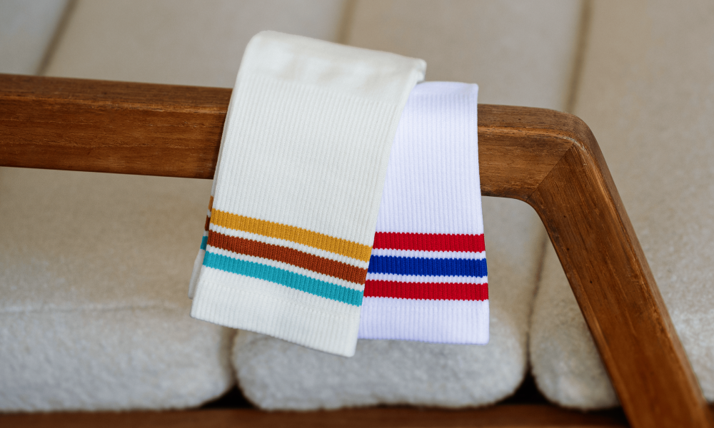 Two pairs of OUTWAY athletic crew socks with colourful stripe designs draped over a wooden chair arm