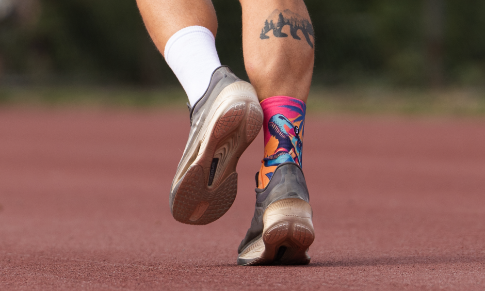 Runner on a track wearing OUTWAY athletic quarter socks with colourful dinosaur pattern